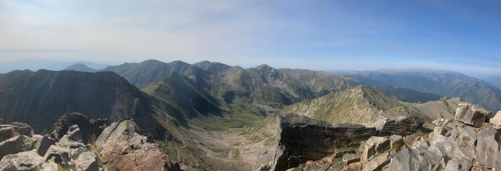 Panorama spectaculaire d'une chaîne de montagnes escarpées avec une vallée verdoyante sous un ciel bleu clair dégagé.